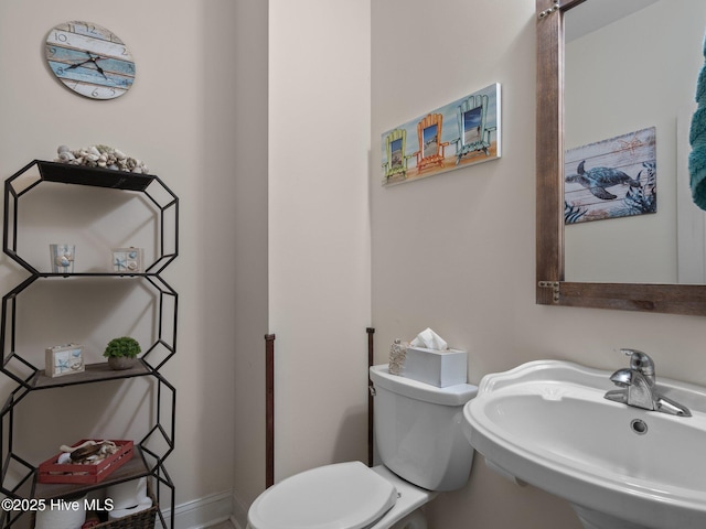 half bathroom with toilet, baseboards, and a sink