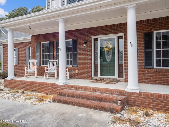 entrance to property featuring brick siding, covered porch, and roof with shingles