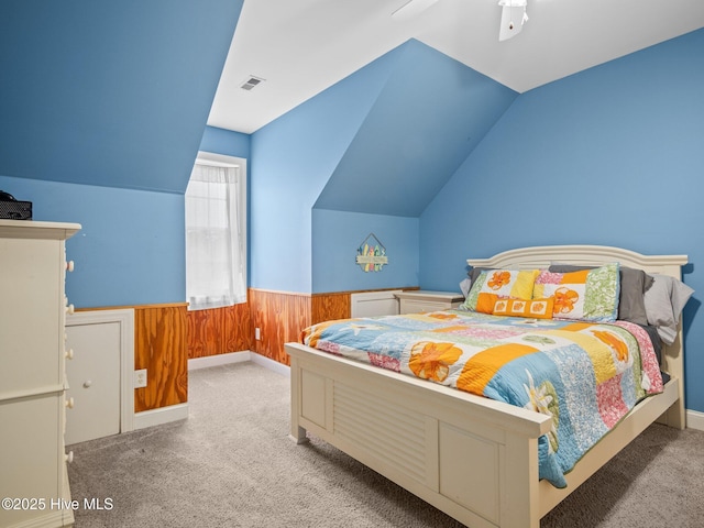 carpeted bedroom with vaulted ceiling, wooden walls, visible vents, and a wainscoted wall