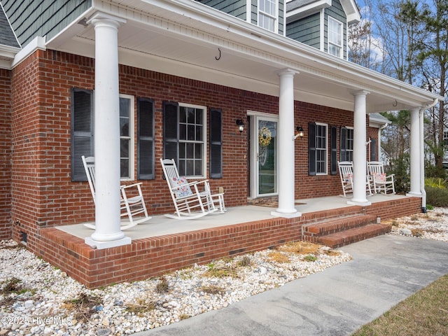 doorway to property featuring a porch and brick siding