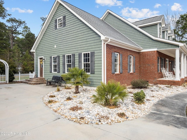 view of side of property featuring covered porch, a shingled roof, and fence