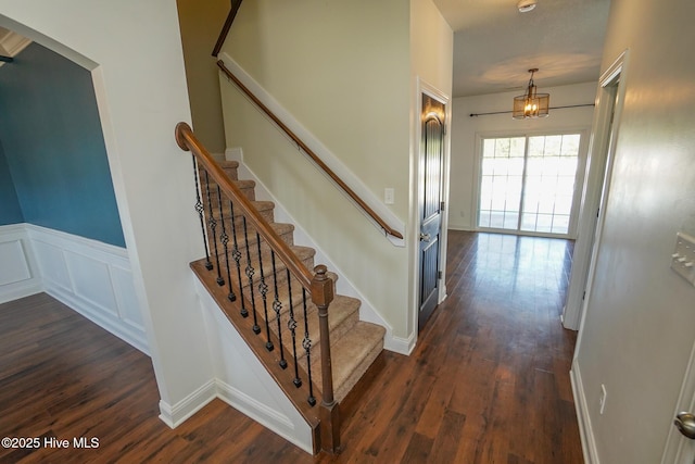 stairs with a decorative wall, wood finished floors, and wainscoting