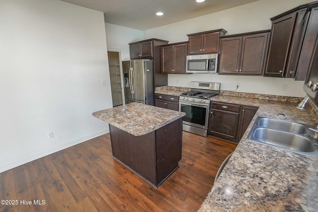 kitchen with a kitchen island, appliances with stainless steel finishes, dark wood-style flooring, dark brown cabinets, and a sink