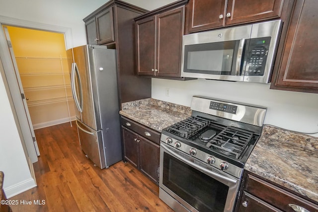 kitchen with stainless steel appliances, dark brown cabinets, dark wood-style flooring, and dark stone countertops