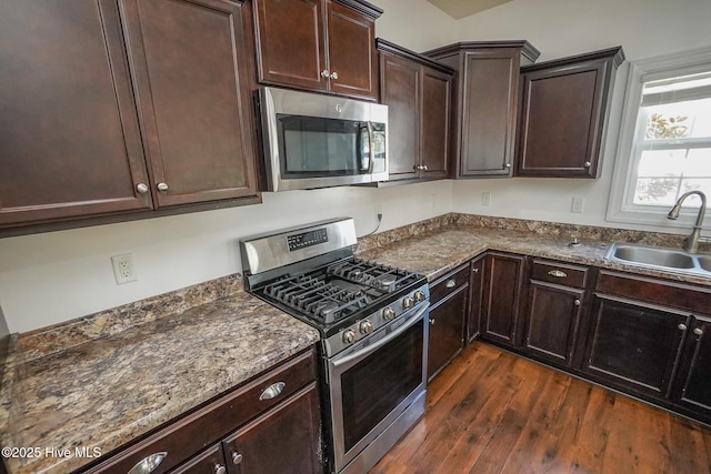 kitchen with stainless steel appliances, a sink, dark brown cabinets, dark stone countertops, and dark wood finished floors