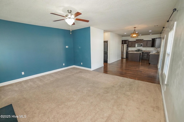 unfurnished living room featuring baseboards, dark carpet, ceiling fan, and a textured ceiling