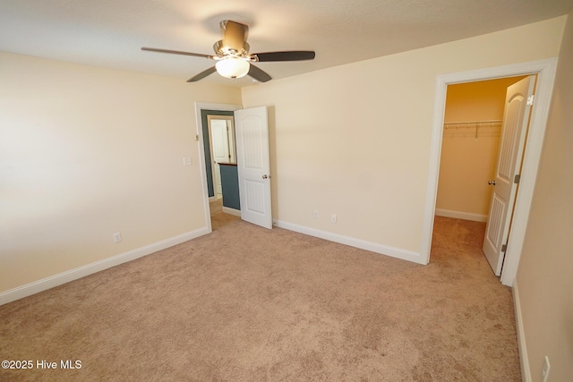 unfurnished bedroom featuring light carpet, a spacious closet, a closet, and baseboards