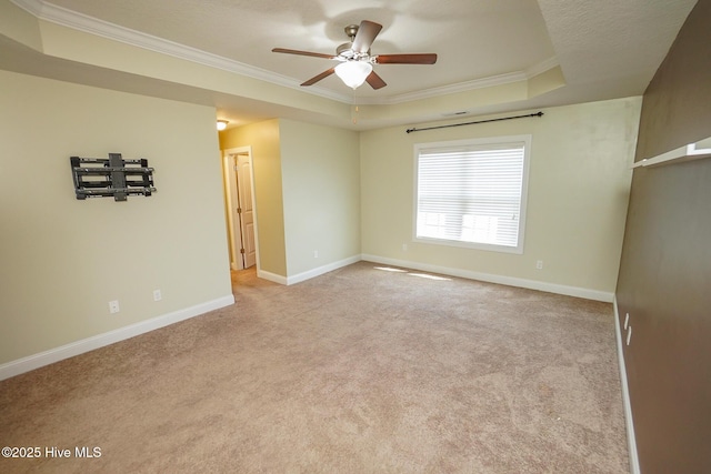 unfurnished room with ornamental molding, a tray ceiling, light colored carpet, and baseboards