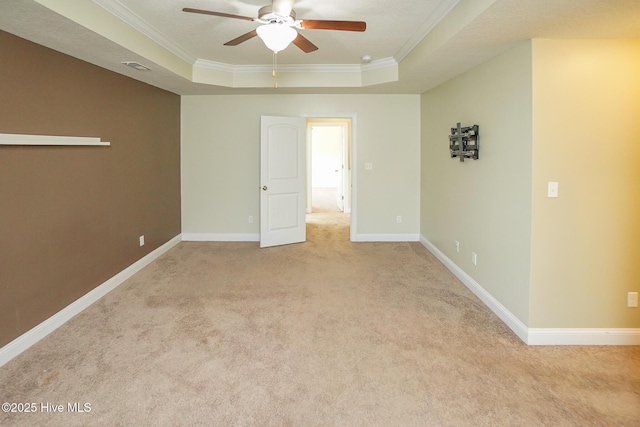 spare room featuring a tray ceiling, carpet, crown molding, ceiling fan, and baseboards