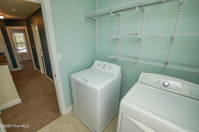 washroom featuring washing machine and dryer, light carpet, light tile patterned flooring, laundry area, and baseboards