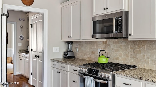 kitchen with stainless steel appliances, dark wood-type flooring, white cabinets, backsplash, and light stone countertops