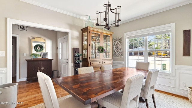 dining room with crown molding, a wainscoted wall, an inviting chandelier, and light wood-style floors