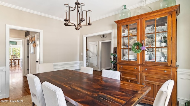 dining area with a wainscoted wall, a decorative wall, an inviting chandelier, ornamental molding, and wood finished floors