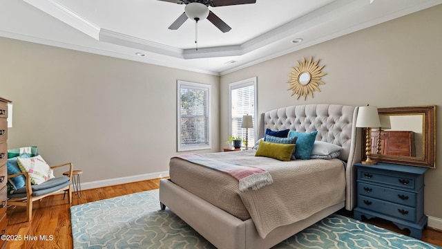 bedroom featuring ornamental molding, a tray ceiling, baseboards, and wood finished floors