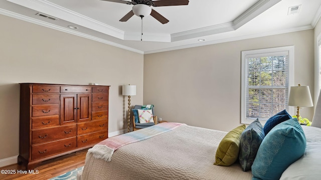 bedroom with a tray ceiling, wood finished floors, visible vents, and baseboards