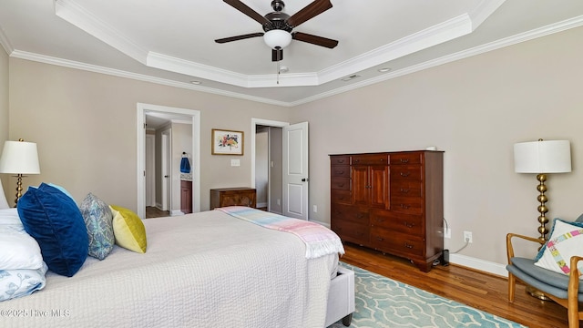 bedroom with a tray ceiling, crown molding, visible vents, wood finished floors, and baseboards