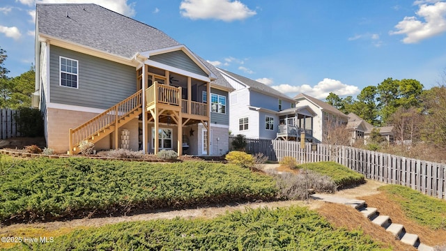 rear view of property featuring a shingled roof, stairway, a fenced backyard, and a sunroom