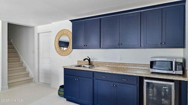 kitchen with wine cooler, stainless steel microwave, blue cabinets, light countertops, and a sink