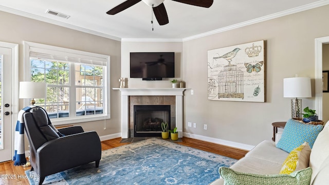 living room with crown molding, a fireplace, visible vents, and wood finished floors