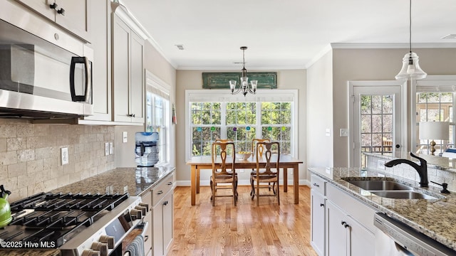 kitchen featuring stainless steel appliances, hanging light fixtures, ornamental molding, a sink, and light wood-type flooring