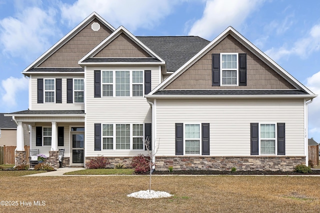 craftsman-style house with stone siding, covered porch, a front yard, and roof with shingles