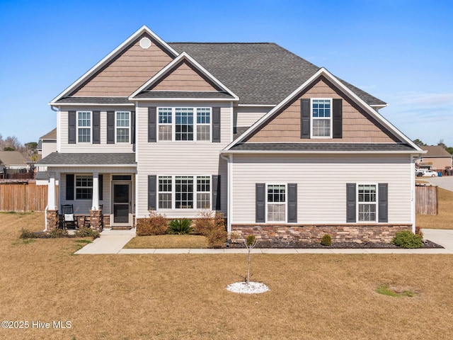 craftsman-style house featuring a front yard, fence, covered porch, a shingled roof, and stone siding