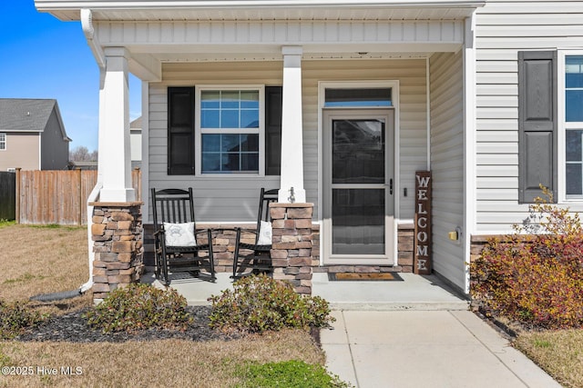 view of exterior entry with covered porch and fence