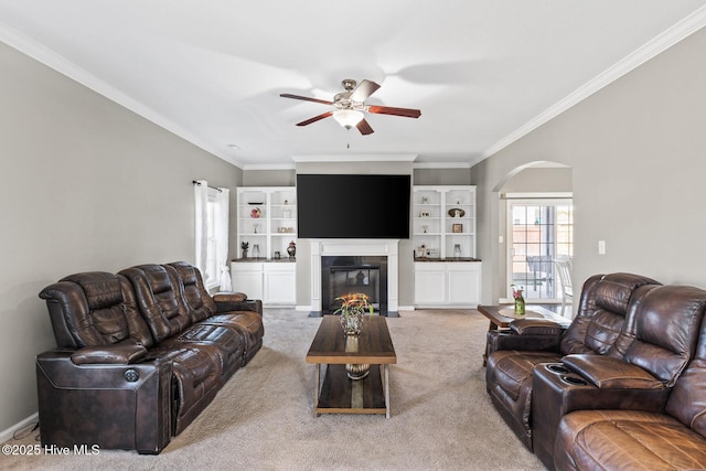 carpeted living area with arched walkways, a fireplace with flush hearth, a ceiling fan, and ornamental molding