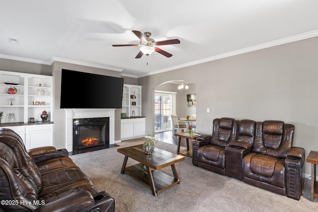 carpeted living area featuring a fireplace with flush hearth, arched walkways, ceiling fan, and ornamental molding