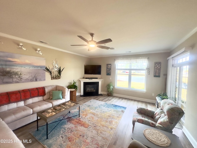 living room featuring a glass covered fireplace, wood finished floors, visible vents, and crown molding