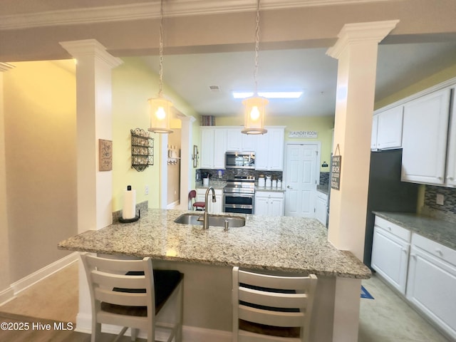 kitchen featuring light stone counters, stainless steel appliances, backsplash, a sink, and ornate columns