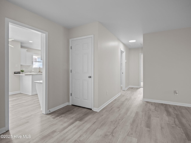 corridor featuring light wood-style floors, baseboards, and a sink