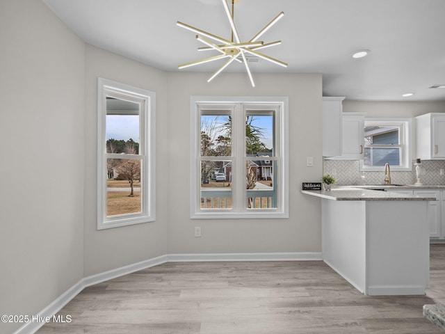 kitchen featuring light wood-style flooring, backsplash, white cabinetry, and a healthy amount of sunlight