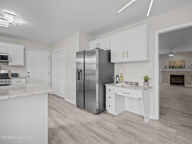 kitchen featuring white cabinetry, light wood-style floors, appliances with stainless steel finishes, tasteful backsplash, and a tiled fireplace