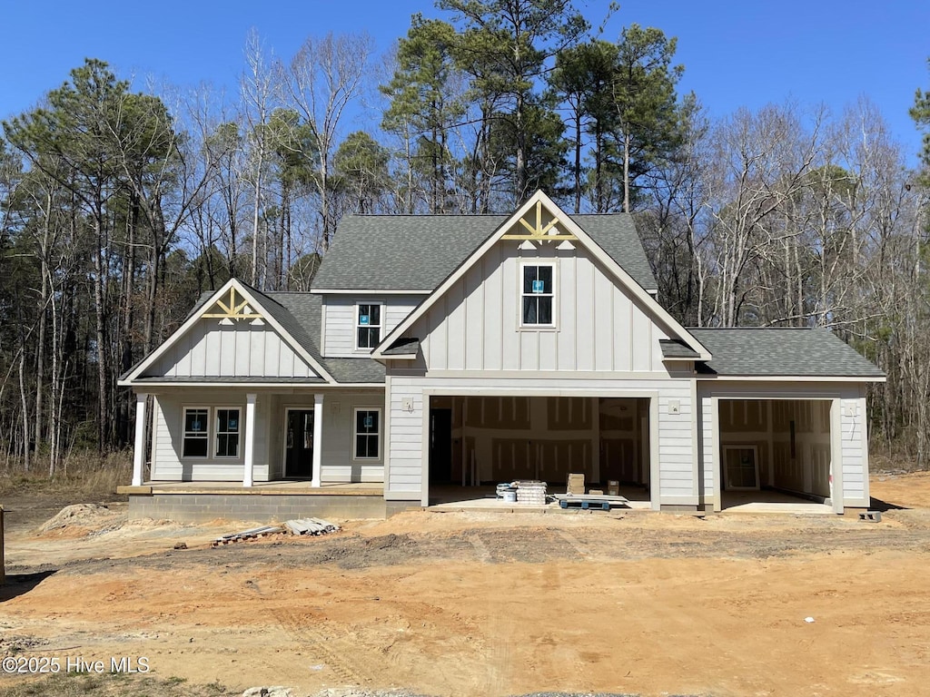 modern farmhouse style home featuring a porch, a garage, a shingled roof, dirt driveway, and board and batten siding