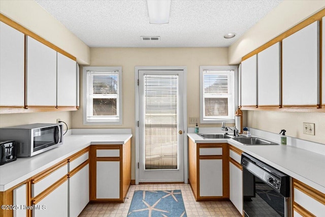 kitchen featuring a textured ceiling, visible vents, light countertops, a sink, and stainless steel microwave