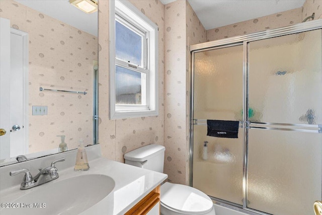full bath featuring vanity, a shower with door, wallpapered walls, and toilet