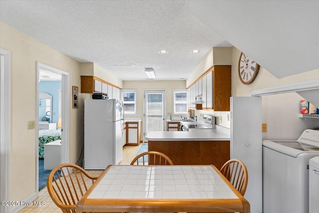 kitchen featuring freestanding refrigerator, a peninsula, washer and dryer, stove, and a textured ceiling