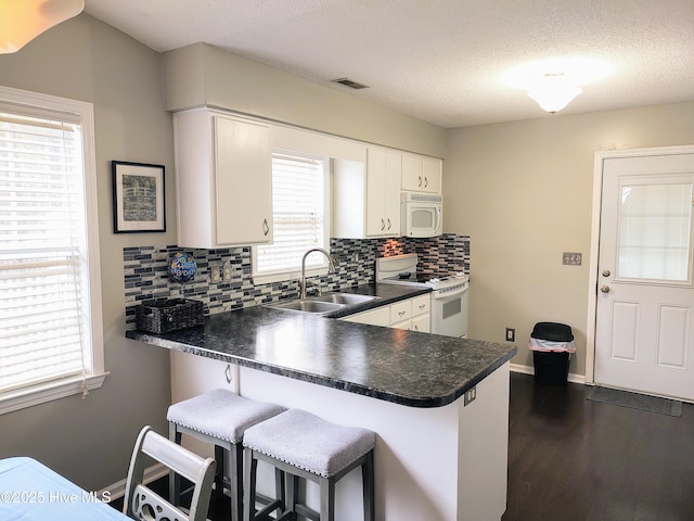 kitchen with dark wood-style floors, dark countertops, a sink, white appliances, and a peninsula