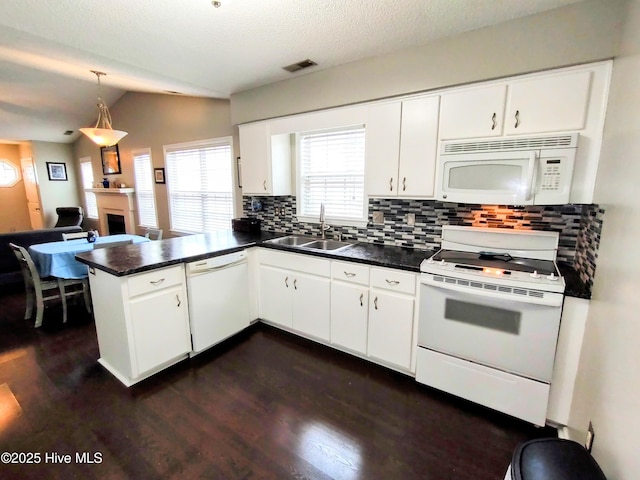 kitchen with a fireplace, dark countertops, a sink, white appliances, and a peninsula