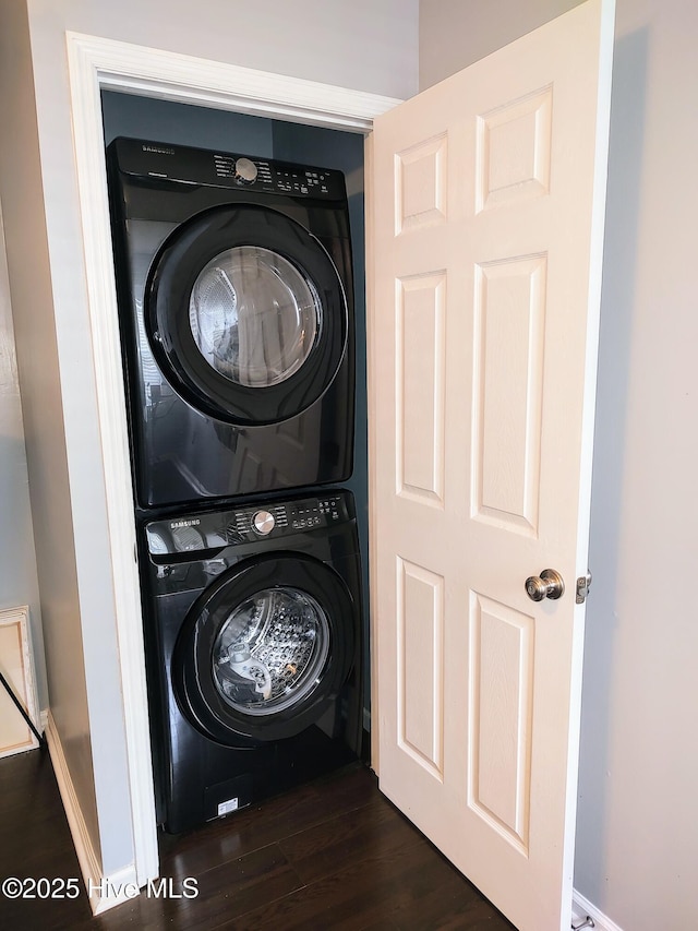 clothes washing area featuring stacked washing maching and dryer, laundry area, and dark wood-type flooring