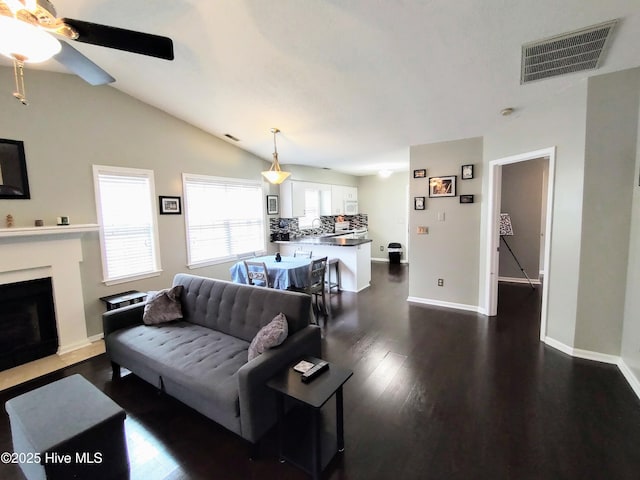 living area featuring a fireplace with flush hearth, lofted ceiling, dark wood-style flooring, and visible vents