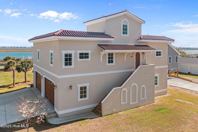 back of house with driveway, a tile roof, stucco siding, an attached garage, and a yard