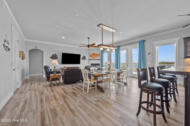 dining area featuring arched walkways, crown molding, light wood-style flooring, and a ceiling fan