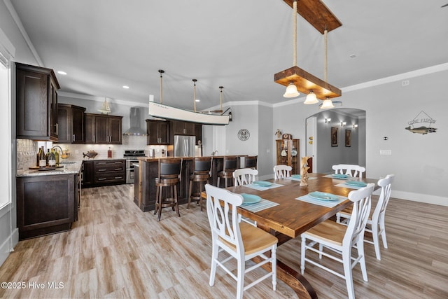 dining room featuring light wood-style flooring, baseboards, ornamental molding, recessed lighting, and arched walkways