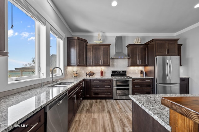 kitchen featuring dark brown cabinetry, a sink, tasteful backsplash, stainless steel appliances, and wall chimney range hood