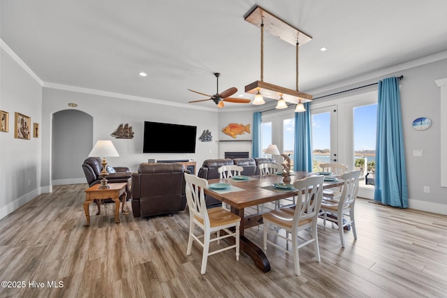 dining room with wood finished floors, baseboards, arched walkways, ceiling fan, and ornamental molding
