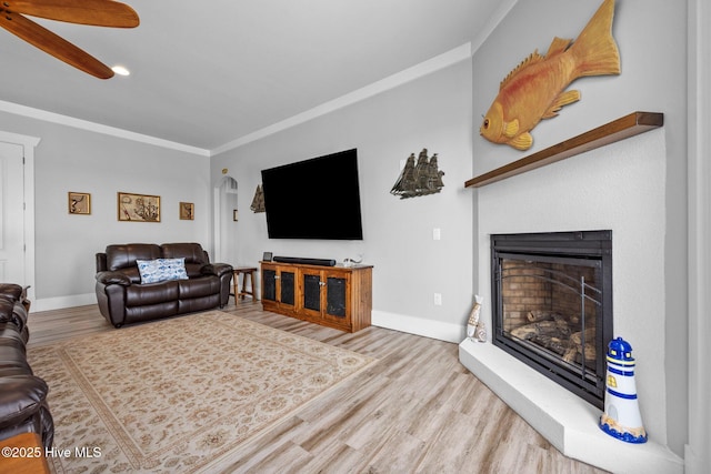 living room with baseboards, ornamental molding, wood finished floors, ceiling fan, and a glass covered fireplace
