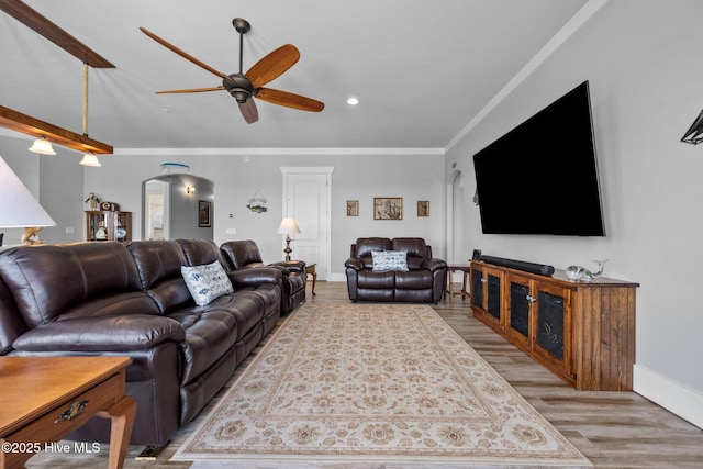 living room featuring crown molding, wood finished floors, baseboards, arched walkways, and ceiling fan