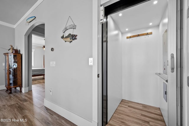 corridor featuring elevator, arched walkways, wood finished floors, and recessed lighting